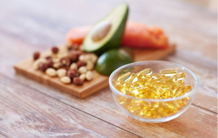 omega 3 rich foods like avocado, nuts, and supplements on a wood table