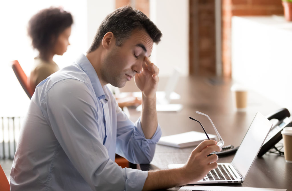 Man in front of a laptop rubbing his eyes because of digital eye strain.