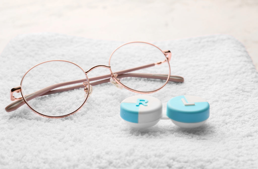 A pair of glasses and contact lens case sitting on a white towel.