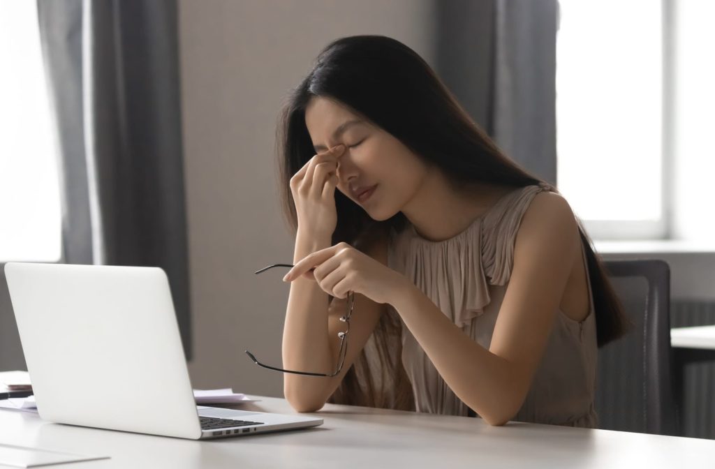 A tired woman with dry eyes takes a break from working on her laptop to close her eyes