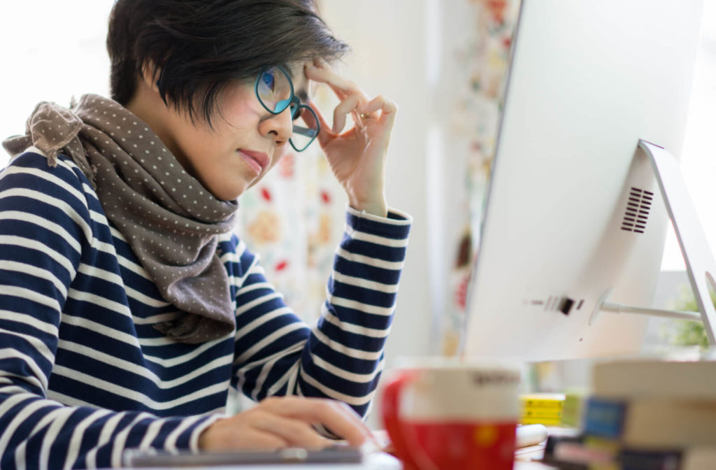 a woman wearing blue light glasses works on her computer