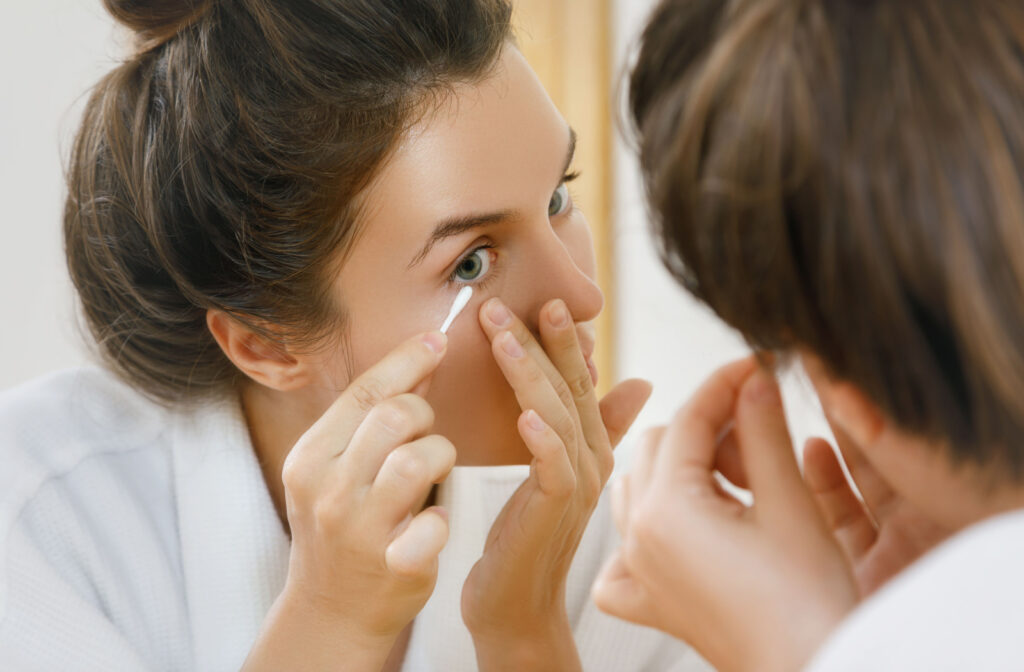 A woman in the mirror is cleaning her eyelid with cotton buds with ZEST for blepharitis.