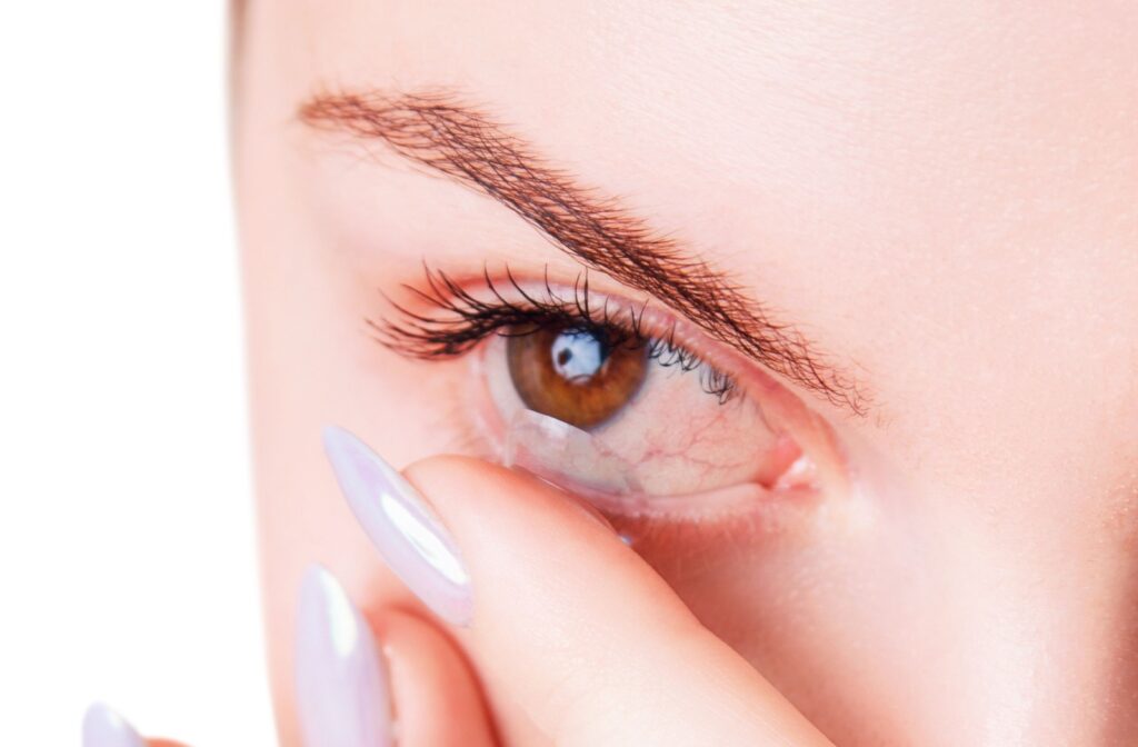 A woman using her left index finger to put a contact lens in her dry and irritated right eye.