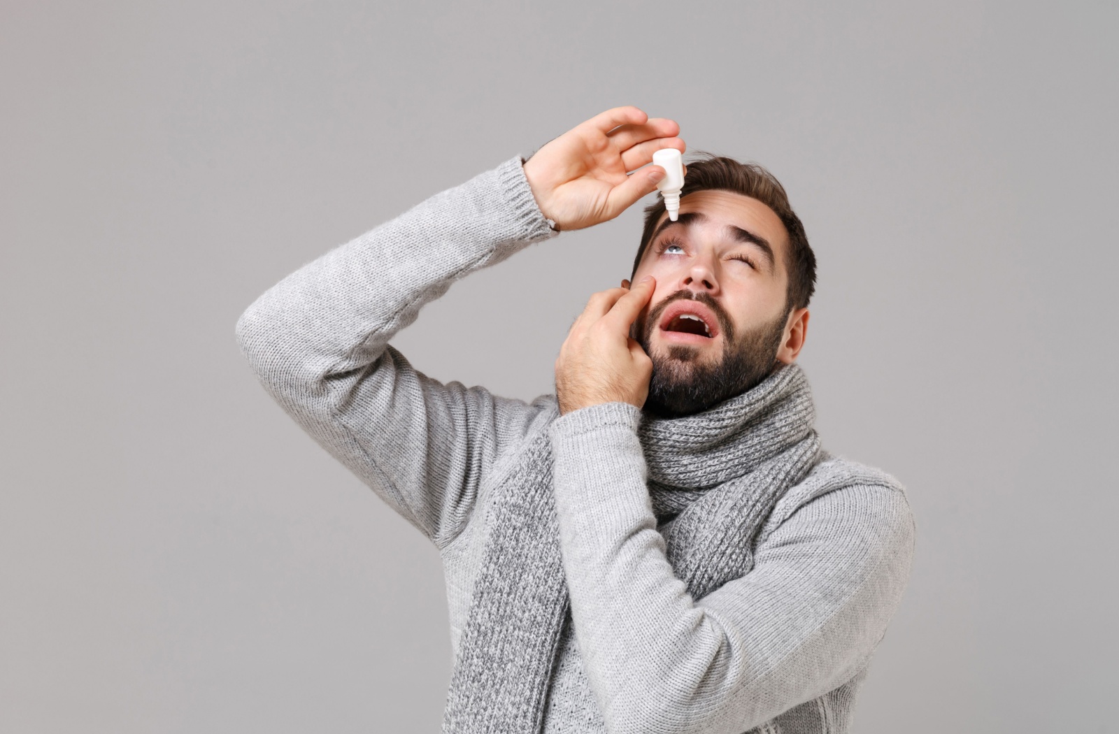 A man holding a bottle of lubricating eye drops over his right eye.