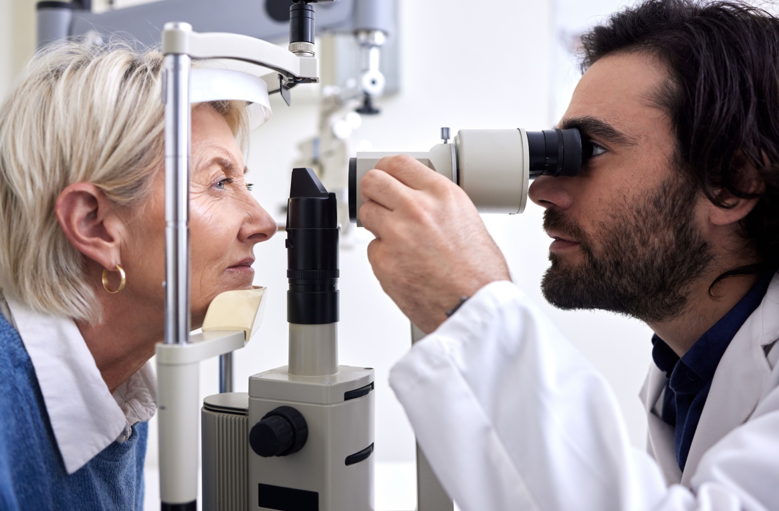 A side-view of an optometrist examining an older patient's eyes to look for diabetes and other conditions.