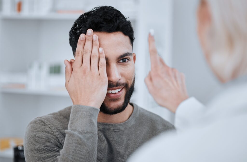 A patient covers an eye with their hand while their eye doctor holds up a single finger to test their eye movement and muscle function.