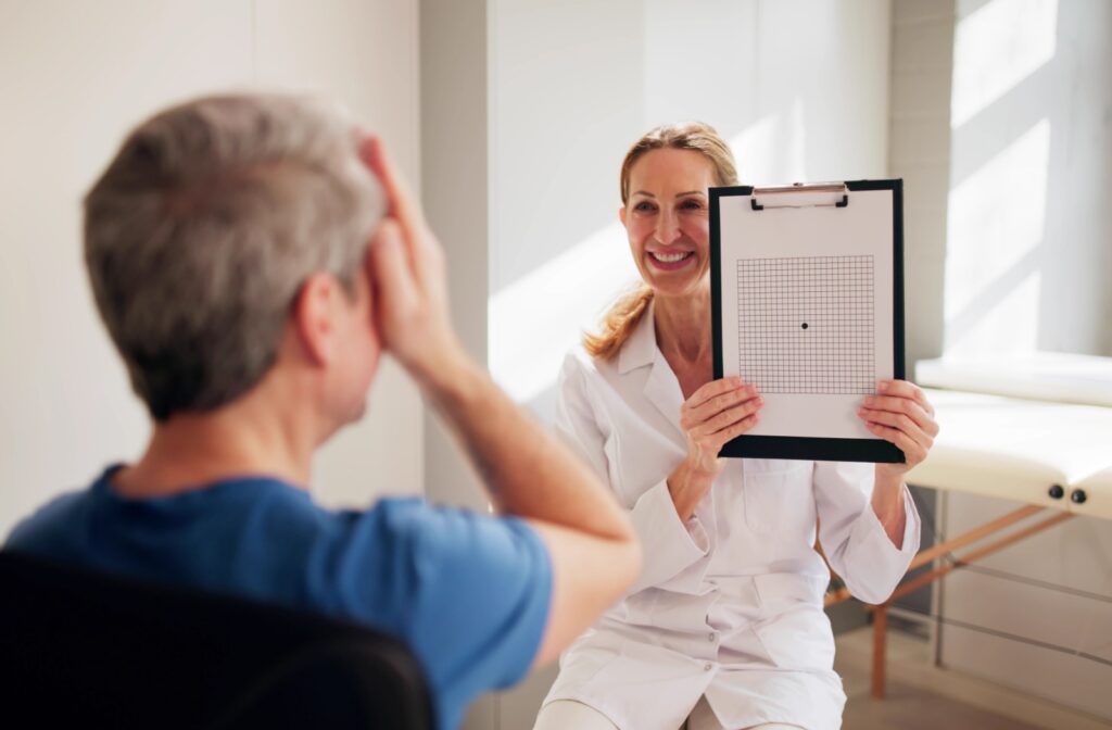 An optometrist smiling during an eye exam while a patient covers one eye.