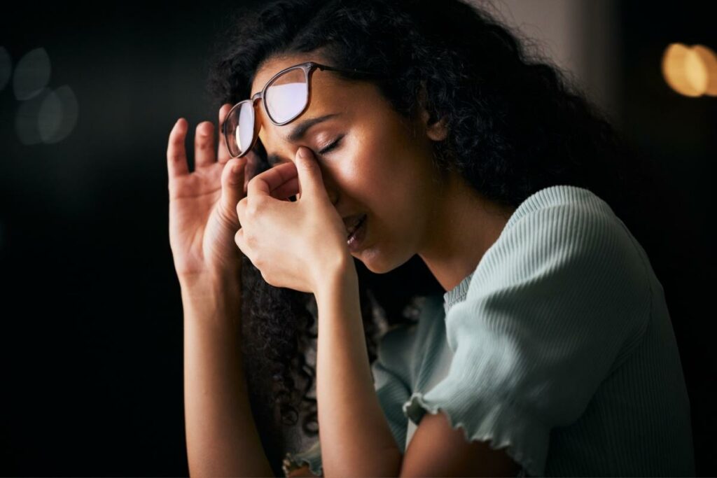Young woman rubbing her eyes with screen glare on her glasses.